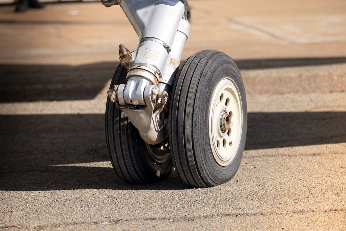 A historic vintage aircraft parked in an aviation hangar undergoing mechanical inspection on its main landing gear tires.
