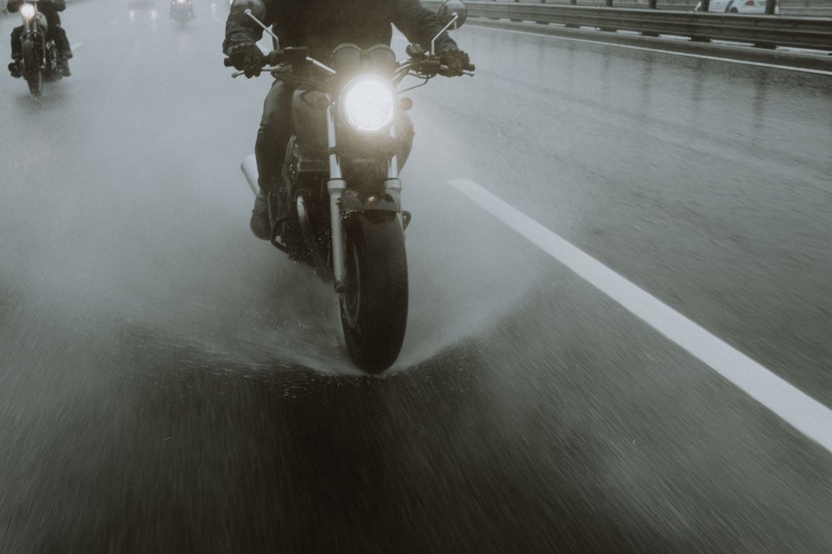 A motorcycle traveling safely across a rain-slicked city street with water splashing off the tire treads.