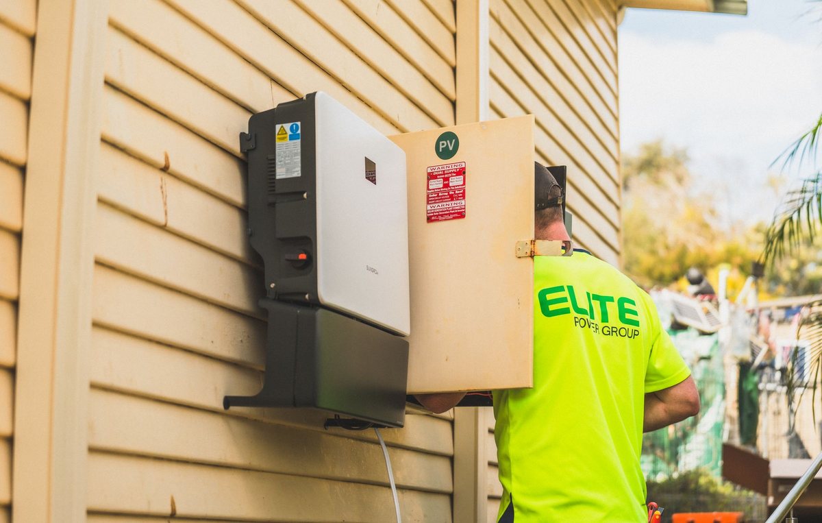 A technician working on rooftop solar brackets and conduit wiring on a modern house.